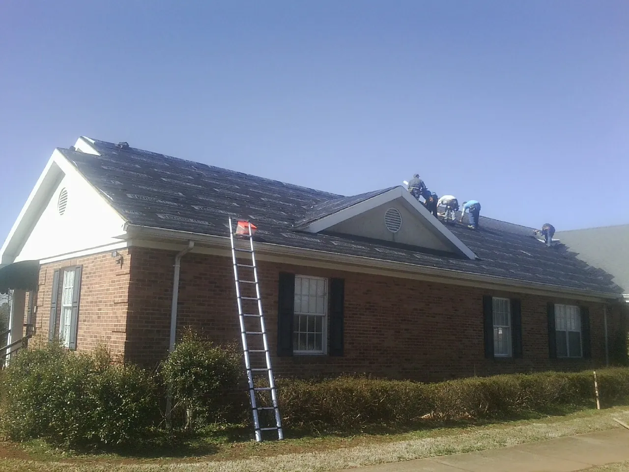 Crew tearing shingles off a brick ranch roof with a ladder set — Metal Roof Repair work by our crew in Alpine