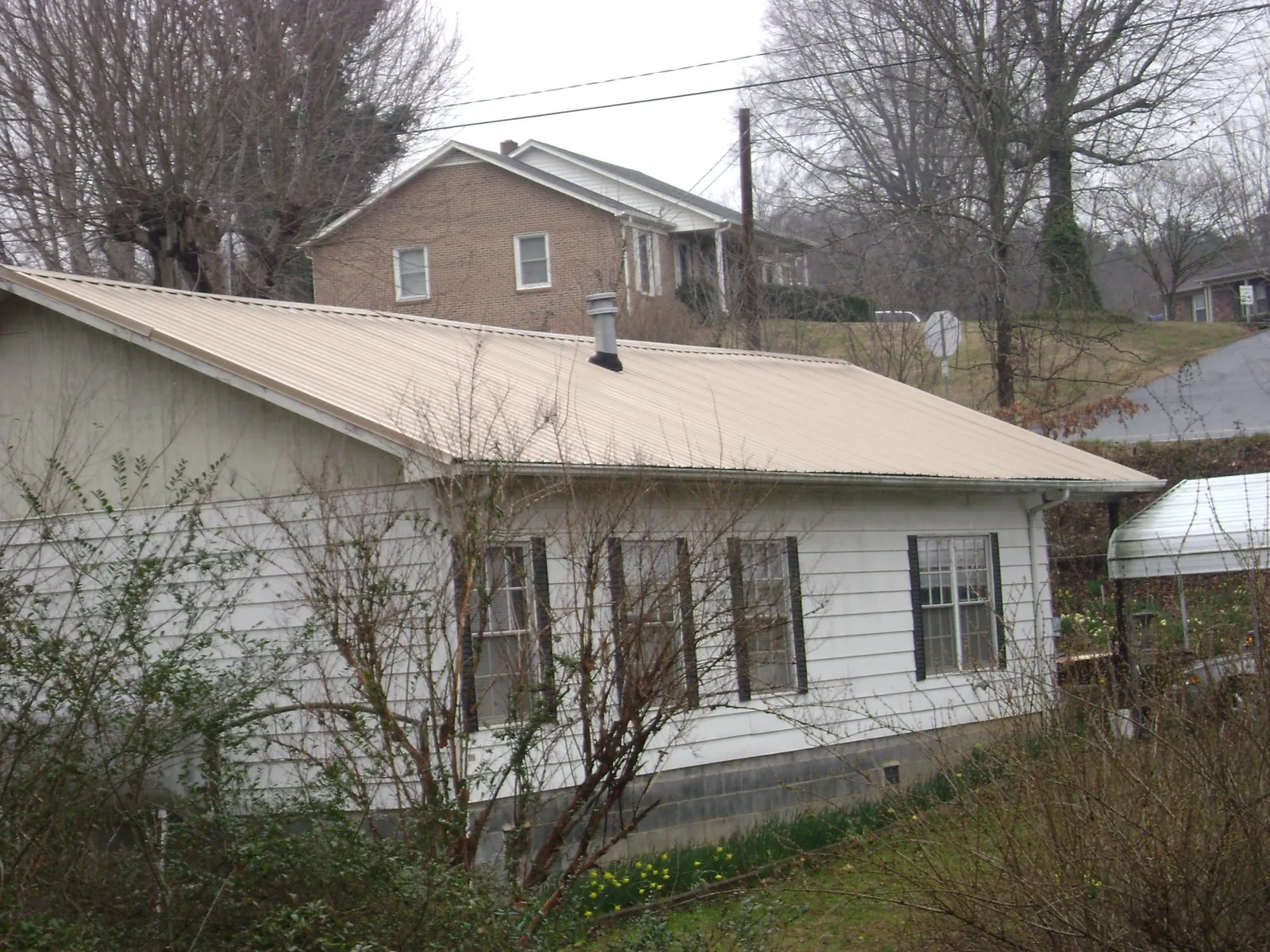 Tan metal roof on a white sided house set into a hillside — Commercial Roofing by Roofing Brothers in Alpine