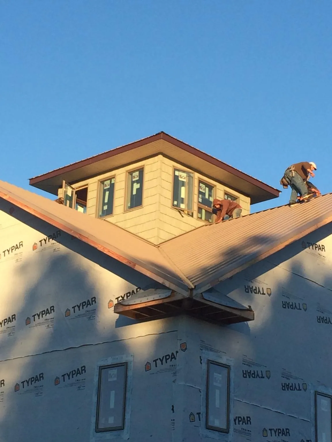 Roofers working around a rooftop cupola on a new metal roof at sunset — Roof Waterproofing in Alpine by Roofing Brothers